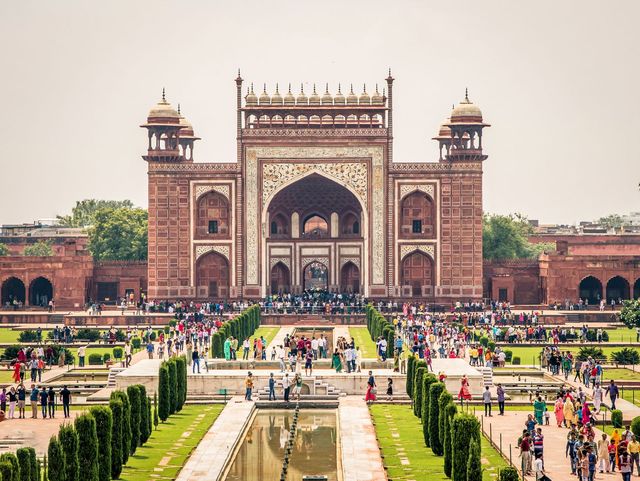 Den stora porten till Taj Mahal i röd sandsten med vit marmor och kalligrafi, med folkmassor och den långa kanalen framför