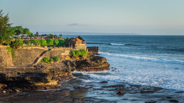 Templet Tanah Lot på sin klippa i havet, med vågor runt om och besökare på klippkanten