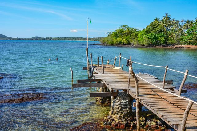 Träpir ut i grunt turkost vatten vid en strand på Koh Mak