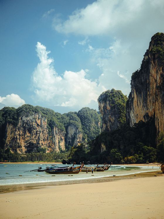 Longtailbåtar i vattenbrynet på Railay West med höga kalkstensklippor bakom